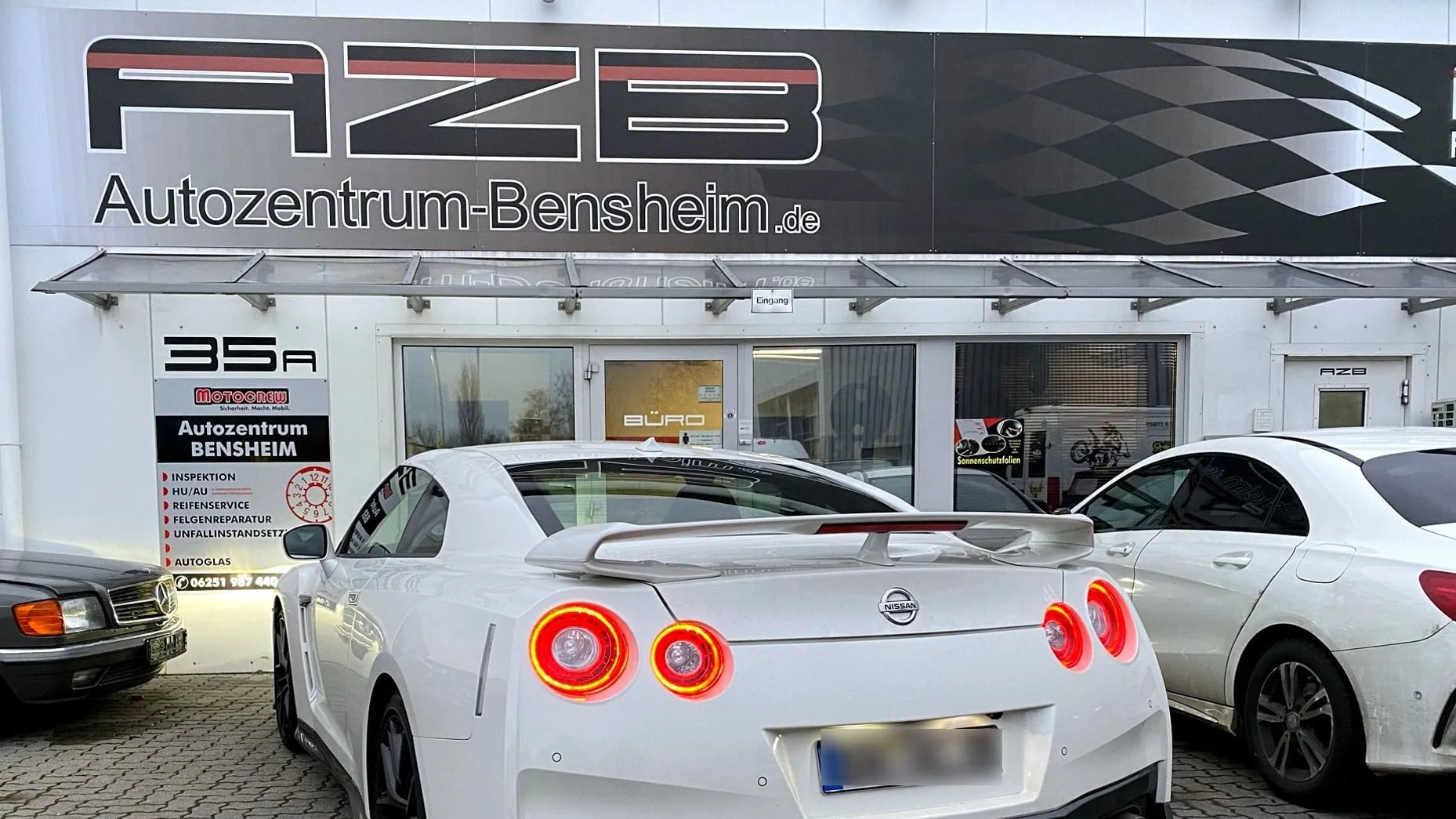 Eingang des Autozentrum Bensheim: großes AZB-Banner über dem Eingang, Hausnummer 35A und die Leistungstafel neben der Tür
