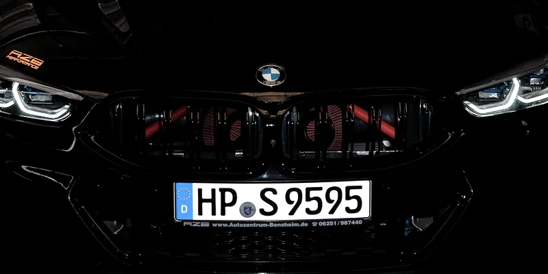 Schwarzer BMW M850i frontal in der abgedunkelten Halle, LED-Scheinwerfer und rot beleuchtete Niere