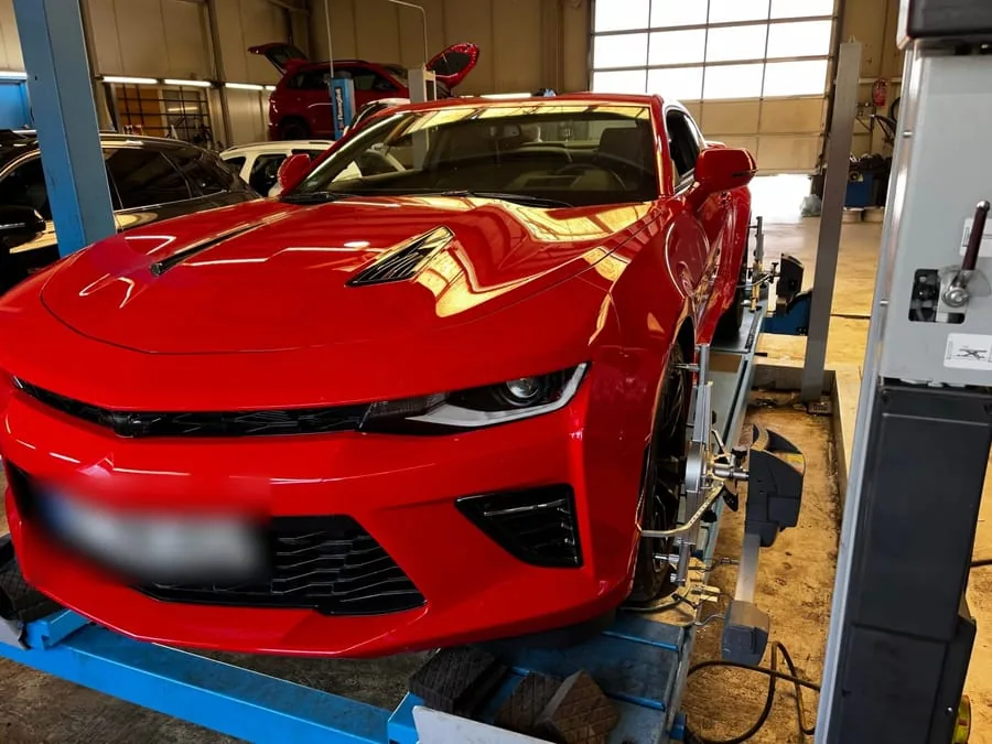 Roter Chevrolet Camaro auf der blauen Achsmessbühne in der Halle, Messkopf am Vorderrad montiert
