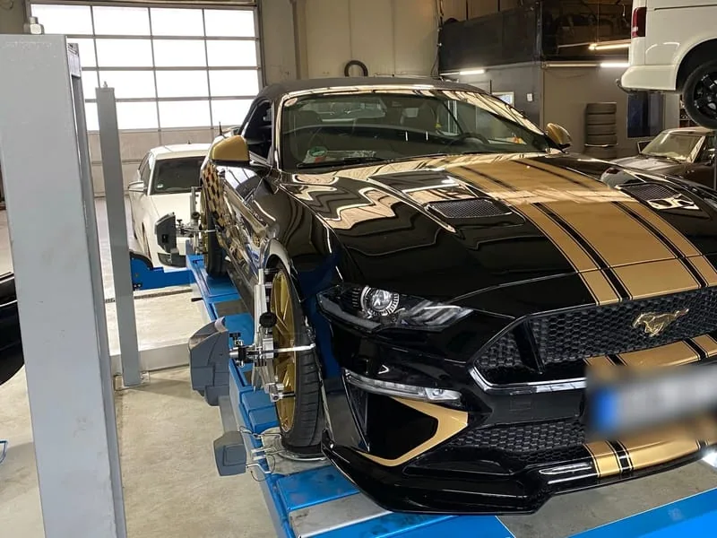 Schwarzer Ford Mustang GT mit goldenen Rennstreifen auf der Hebebühne.