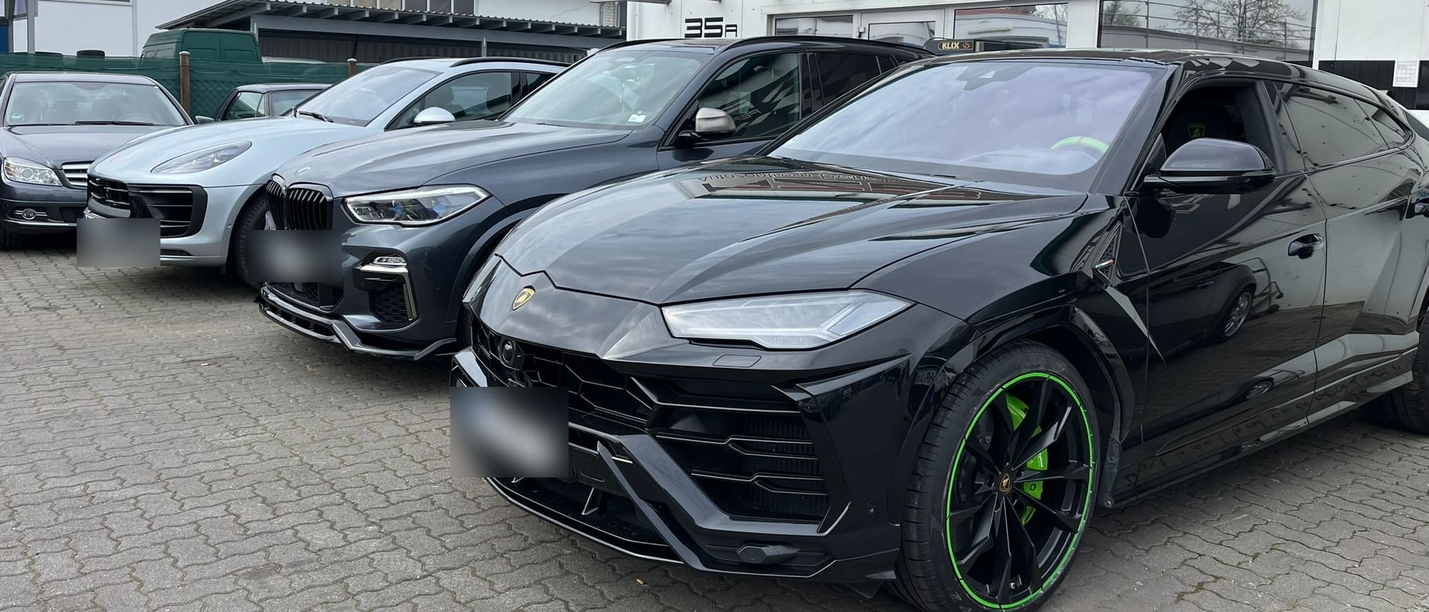 Schwarzer Lamborghini Urus mit grünen Bremssätteln neben BMW X5 und Porsche Macan auf dem Hof des Autozentrum Bensheim.