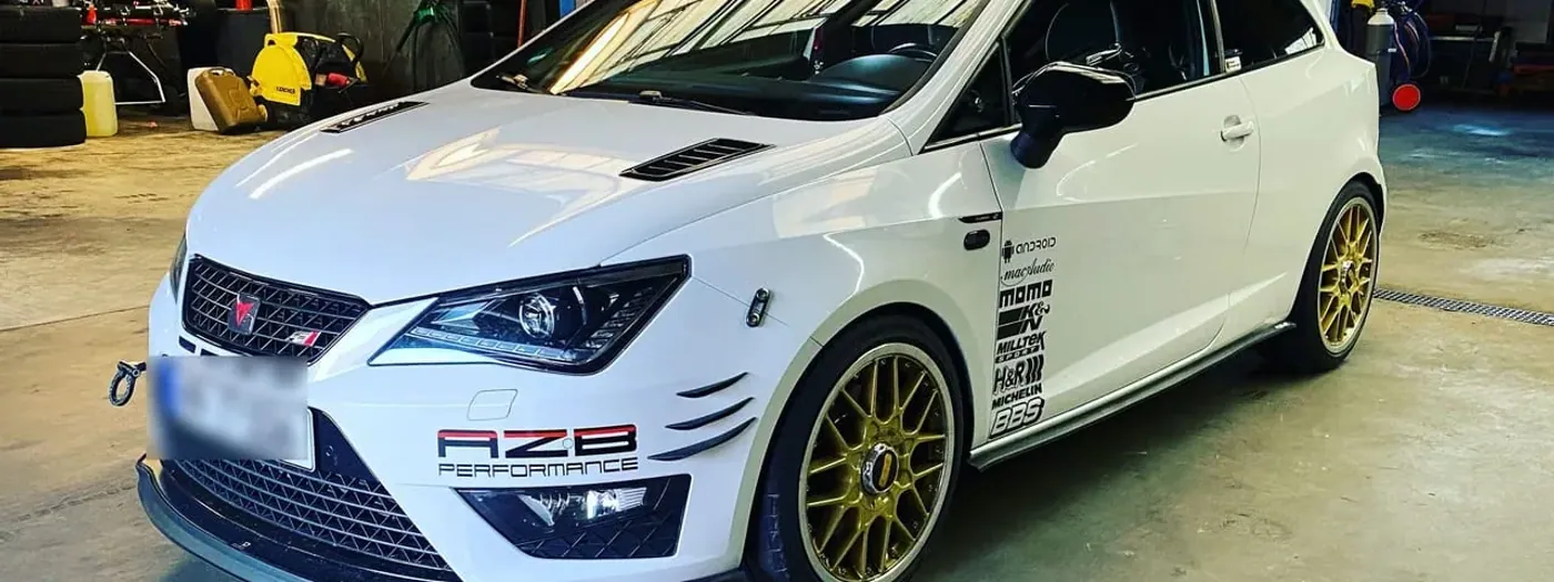 Tiefergelegter weißer Seat Ibiza Cupra mit AZB-Performance-Schriftzug auf der Frontschürze, Frontsplitter und goldenen BBS-Felgen in der Werkstatthalle in Bensheim